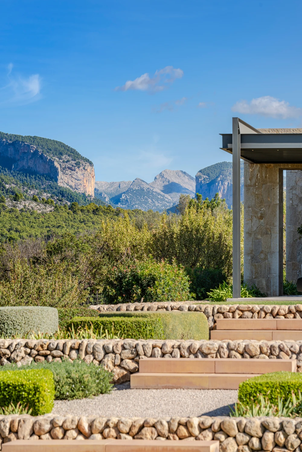 Moderna villa de piedra en Mallorca con jardines aterrazados y vistas panorámicas a la montaña.